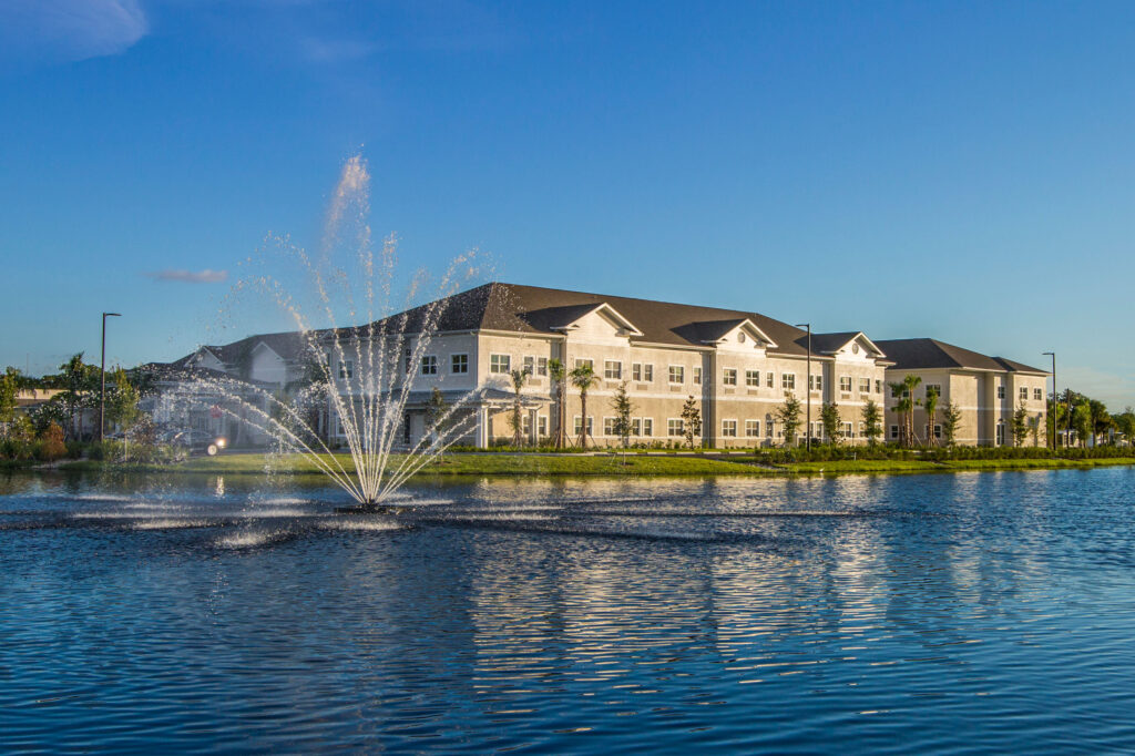 Heritage Oaks at Englewood building standing in the foreground of the lake with a fountain in the middle of it.