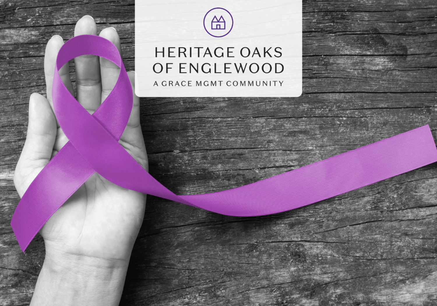 Purple awareness ribbon resting on a cupped hand with a Heritage Oaks of Englewood sign in the background