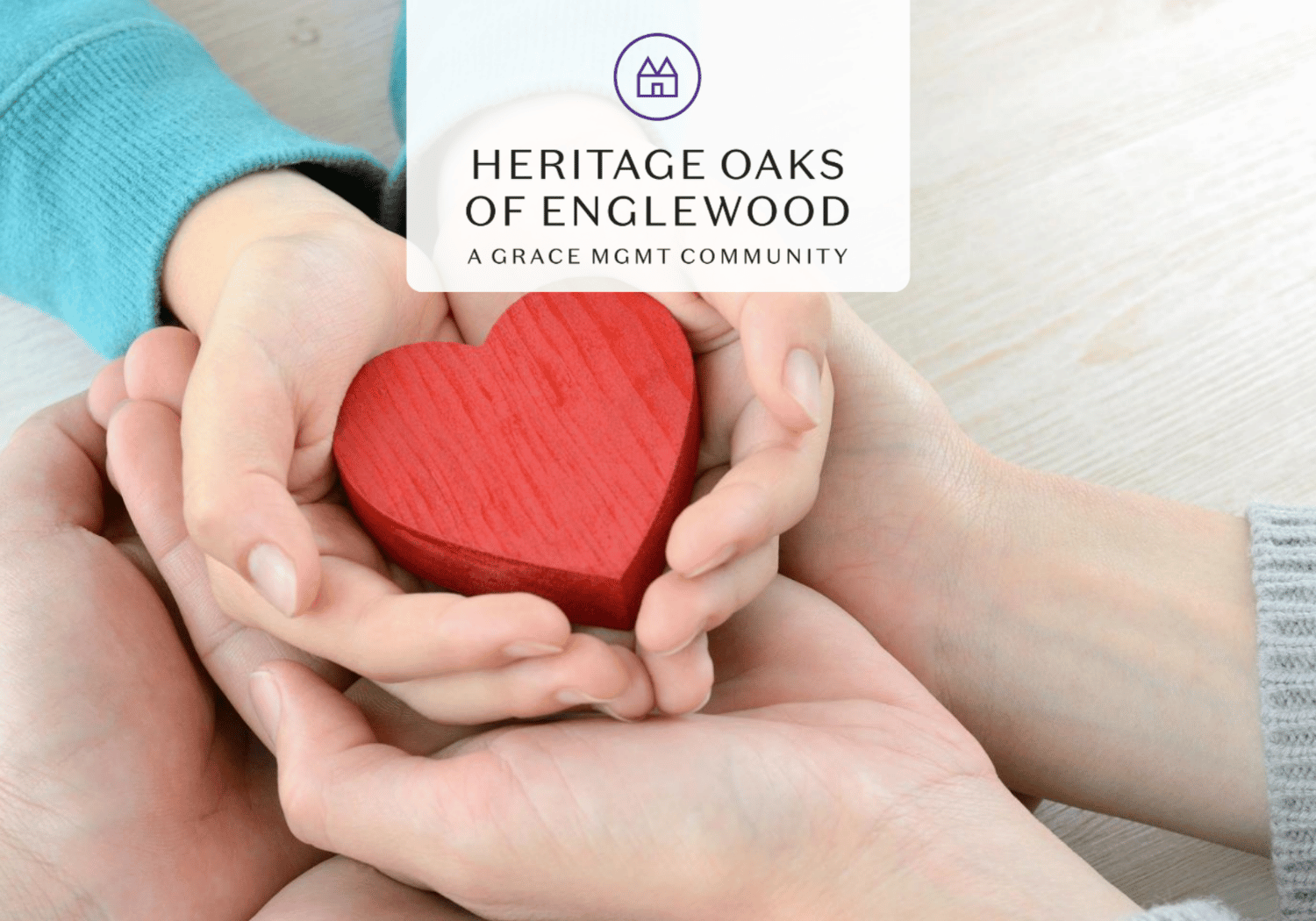 Hands gently cupping a red wooden heart, symbolizing care and support for Heritage Oaks of Englewood.